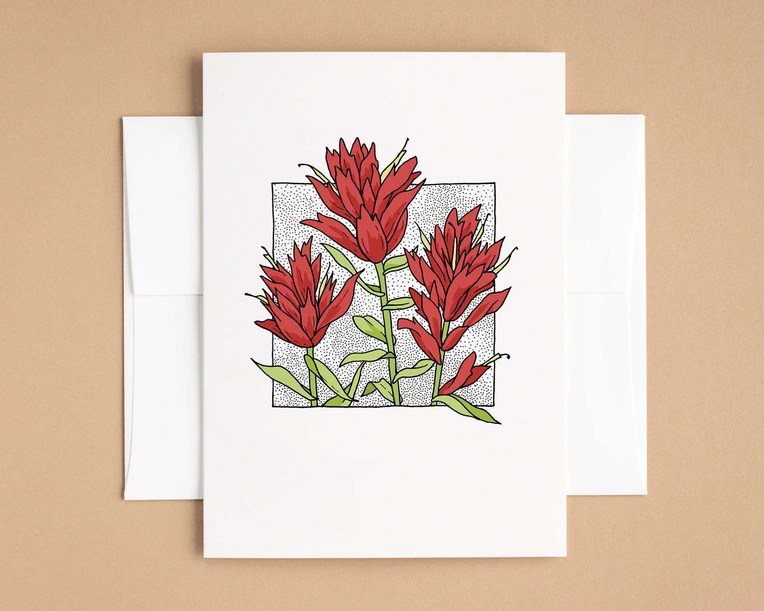 A vertical white card depicts three tall red flowers. The card sits on top of a white envelope, which lies on top of a brown backdrop.